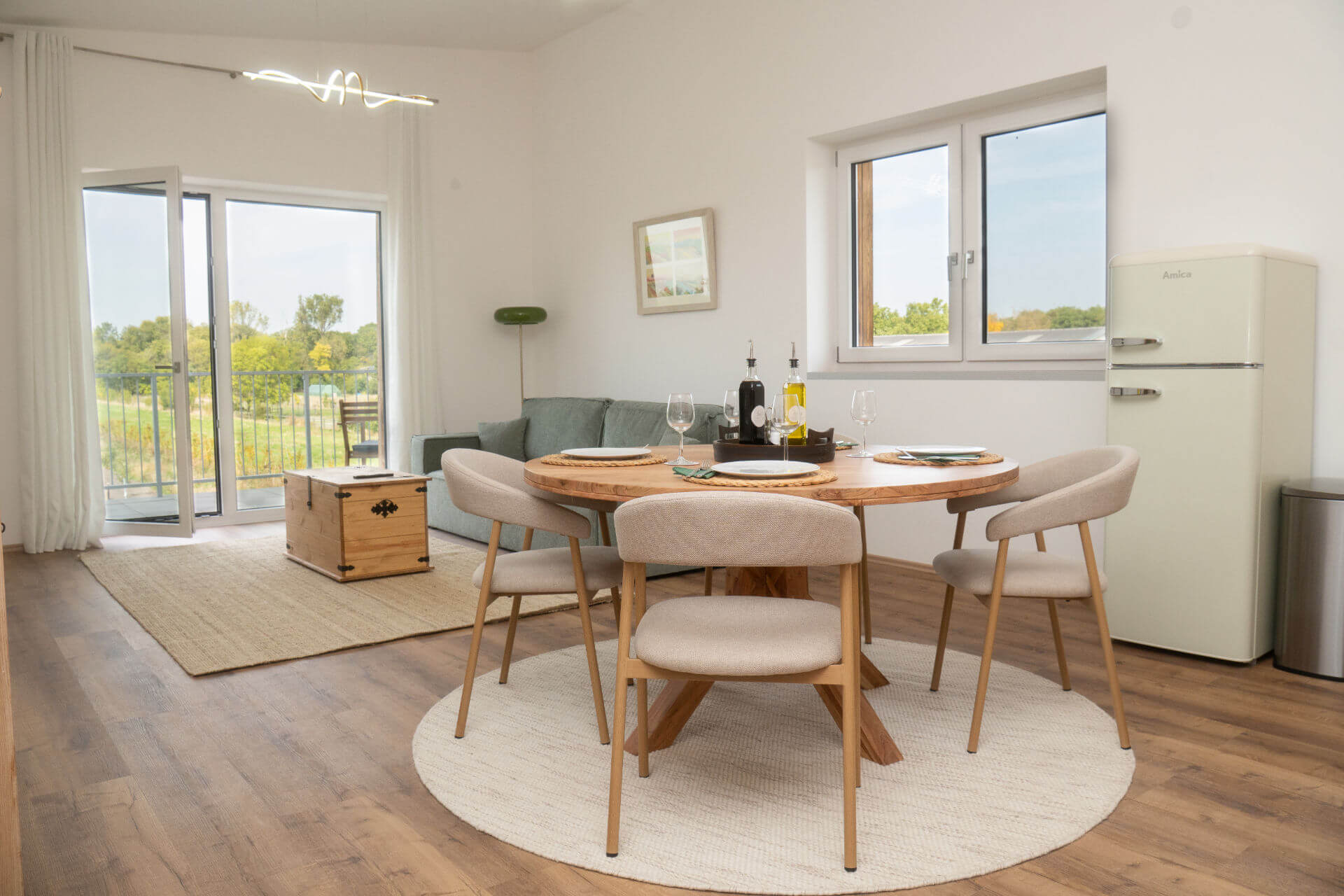 Ess- und Wohnbereich mit rundem Holztisch, grünem Sofa und Blick auf die Weingärten